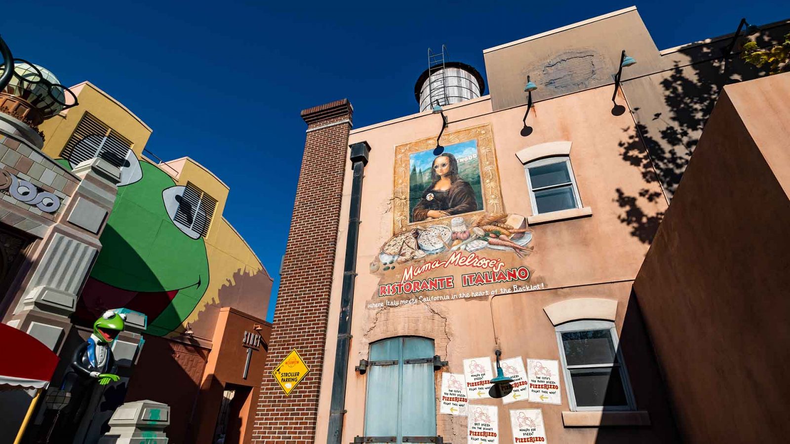 Back Wall of Mama Melrose’s Ristorante Italiano in Disney World Hollywood Studios that features a pop-art depiction of the Mona Lisa in sunglasses and the back of  the Muppets 3D attraction gift shop can be seen